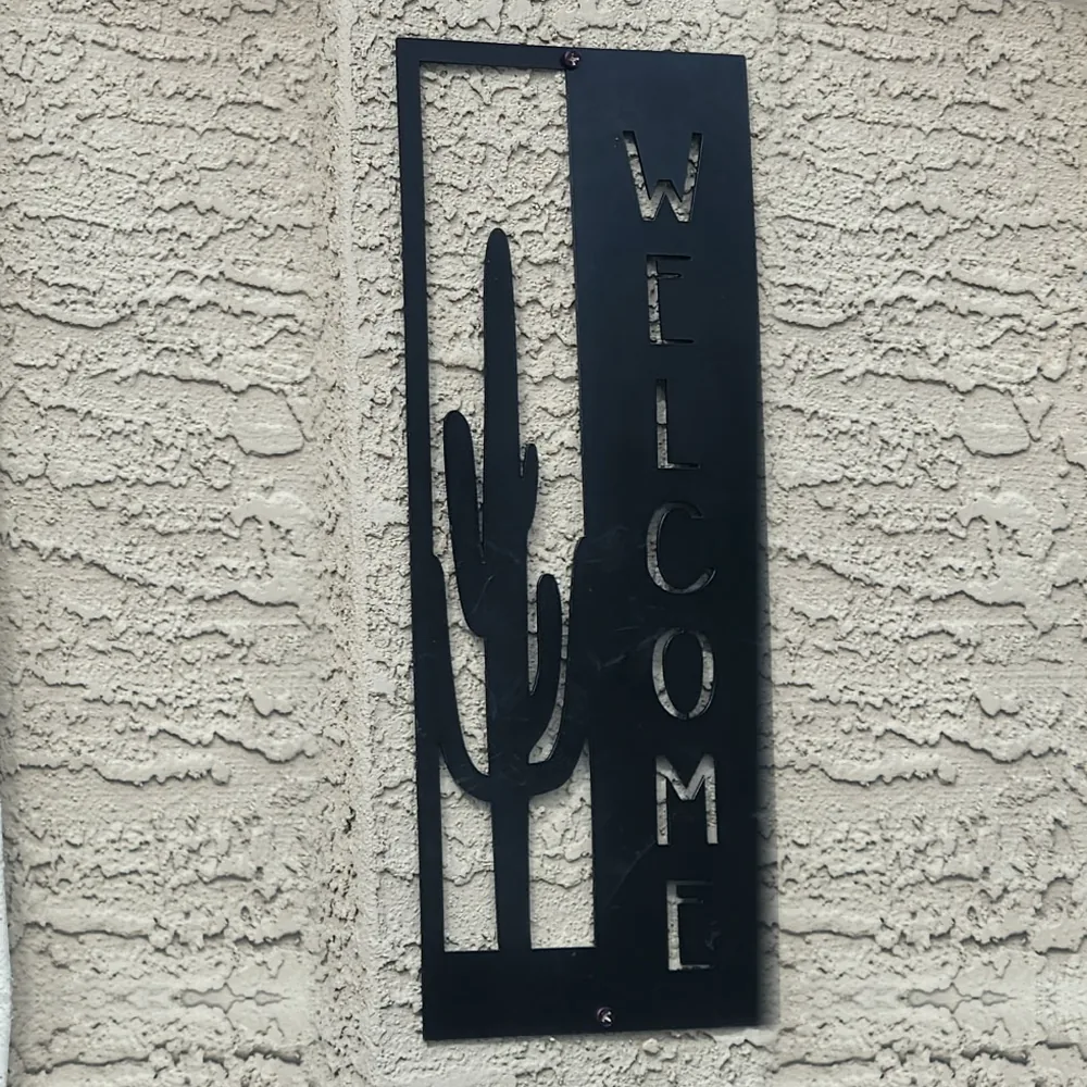 Black steel WELCOME sign with a saguaro cactus, hung on stucco.