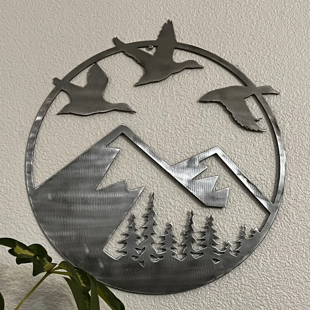 Raw steel round with ducks flying over mountains and pine trees.