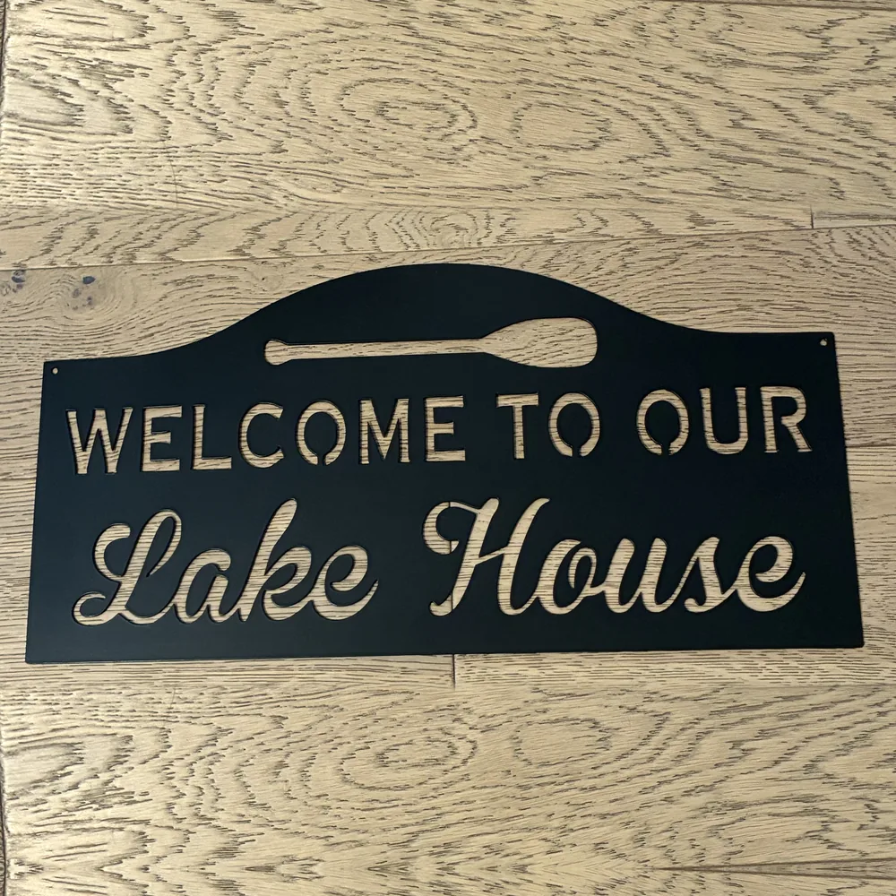 Black steel Welcome to Our Lake House sign with a canoe paddle.