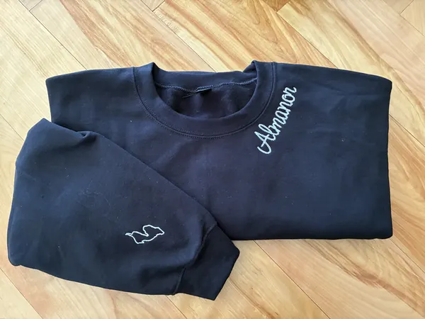 Black sweatshirt with Almanor script by the collar and a lake outline on the sleeve