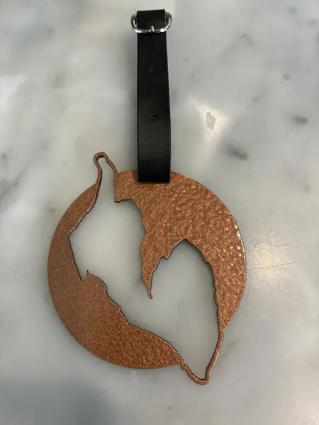 Round hammered copper-finish bag tag with a lake cutout and a leather strap