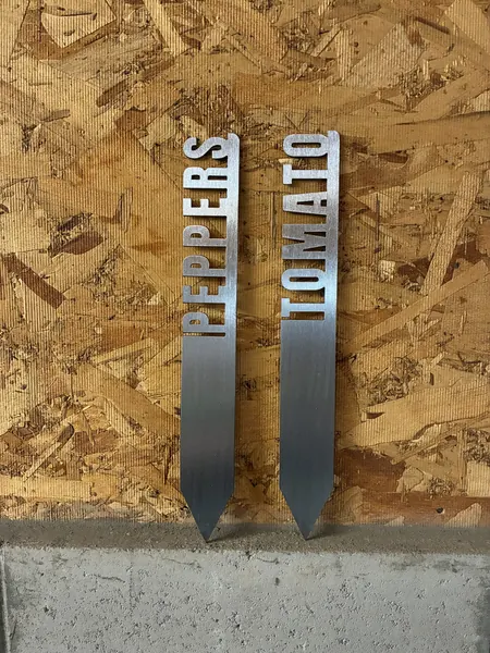 Two brushed steel garden stakes reading PEPPERS and TOMATO